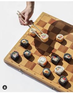 sushi on a chess board with chopsticks being held by someone's hand