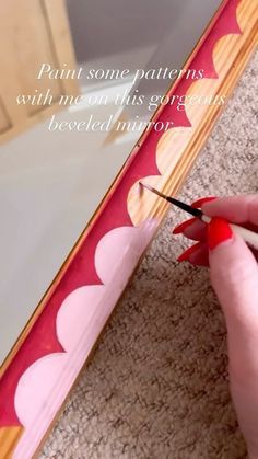 a woman is painting the edge of a mirror with red acrylic paint on it