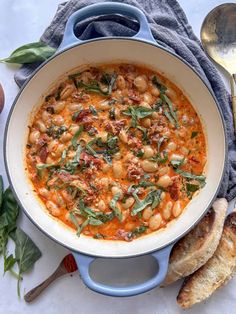 a blue pot filled with beans and spinach next to bread