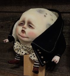 a doll with white hair wearing a black jacket and polka dot dress on top of a wooden block