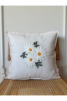 a white pillow with daisies on it sitting on a wicker chair next to a wall