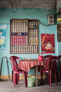 two red chairs sitting at a table in front of a wall with cans on it