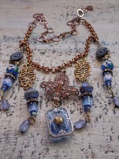 An assemblage of vintage components in a Bohemian style. The central assembled pendant is a vintage to antique fleur dis lis shape copper over brass component to which I've added a vintage German glass intaglio of the Eiffel Tower on the back. It suspends an Art Deco faceted blue glass cabochon in a filigree silver setting. Originally, this pendant would have had a rhinestone in the center, but it was missing, so I've added a gold plated brass filigree bead cap as a focal and to tie it in with the other brass elements in the design. Accompanying pendants are vintage Czech glass buttons, vintage Czech atlas glass and fire polished tulip shaped beads, Japanese 1930s glass beads and vintage lampwork beads with floral detail along with vintage caps and rhinestone rondelles. Length can be adjus Vintage Assemblage Jewelry, Found Object Jewelry, Brass Filigree, Vintage Assemblage, Assemblage Necklace, Mixed Media Jewelry, Necklace Ideas, Repurposed Jewelry, Assemblage Jewelry