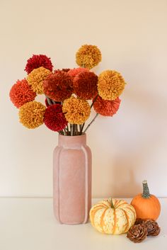 a pink vase filled with lots of colorful flowers next to pumpkins and pine cones