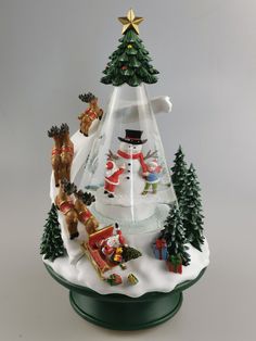 a glass christmas tree with santa claus and other holiday decorations on the top, in front of a grey background