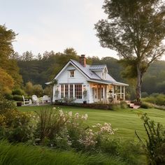 a white house sitting in the middle of a lush green field next to a forest