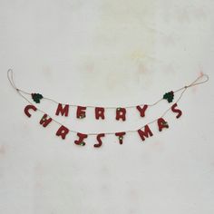 a merry christmas banner hanging on the wall with red letters and holly leaves attached to it