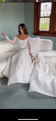 a woman in a white wedding dress sitting on a couch with her hand out to the side