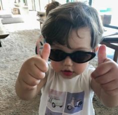 a little boy wearing sunglasses giving the thumbs up