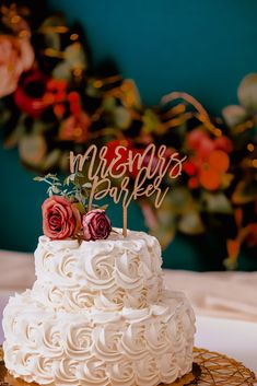 a wedding cake with white frosting and two red roses on top is sitting on a gold plate