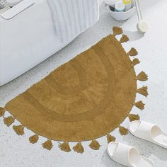 a brown rug with tassels on the floor next to slippers and bathtub