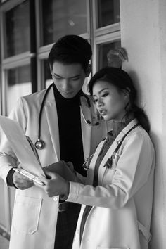 a man and woman in white coats looking at something on a clipboard with stethoscopes