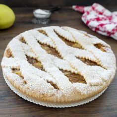 an apple pie with powdered sugar on top sits on a table next to two apples