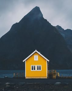 a yellow house sitting on the side of a lake with mountains in the back ground