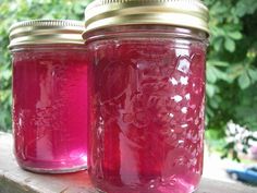 three jars filled with pink liquid sitting on top of a wooden table next to trees