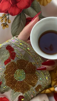 a woman's hand holding a cup of coffee on top of a floral print table cloth