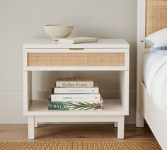 a white nightstand with books on it and a bowl sitting on top of the end table