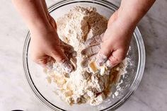 two hands are kneading ingredients in a glass bowl on a marble countertop