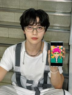 a boy with glasses holding up a cell phone in front of his face and wearing suspenders