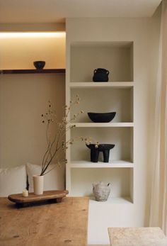 a wooden table topped with white shelves filled with vases and bowls next to a window