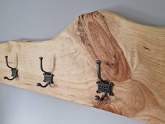 three coat hooks are attached to a wooden wall mounted coat rack with wrought iron handles