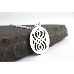 a silver pendant with an intricate design on it sitting on top of a black rock