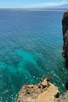 a man standing on top of a cliff next to the ocean with clear blue water