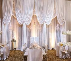 an elegant wedding setup with white linens and flowers on the head table, along with drapes