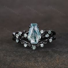 a ring with an aqua green stone surrounded by leaves and stones on the sides, sitting on a dark surface