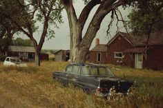 an old car sitting in the middle of a field next to a tree and house