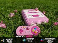 a pink nintendo game boy sitting on top of a lush green grass covered field next to a video game controller