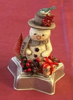 a small snowman sitting on top of a cake pan with christmas decorations around it