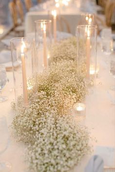 the table is set with candles and baby's breath centerpieces on it