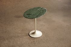 a green marble topped table sitting on top of a cement floor next to a white pedestal