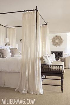 a bedroom with four poster bed and white drapes