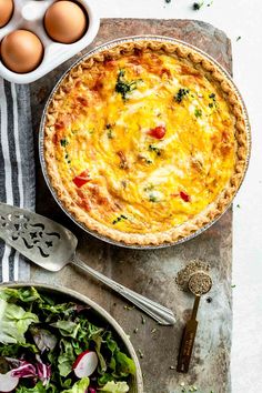 an overhead view of a quiche, salad and eggs on a table with utensils