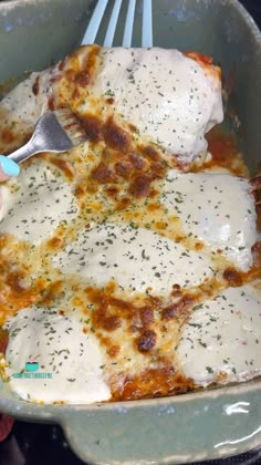 someone is holding a fork over a casserole dish with cheese and sauce on it