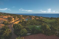 an aerial view of a golf course near the ocean with trees and houses in the foreground