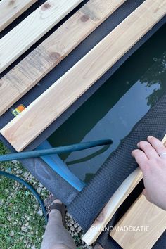 A wood-slatted stock tank pool cover is rolled back, and a garden hose is inside the pool to fill it. In Ground Stock Tank Pool, Cowboy Pools, Cattle Trough, Homemade Pools