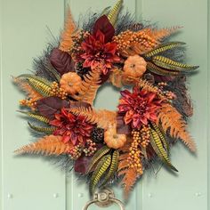 a wreath hanging on the front door with autumn leaves and flowers in it's center