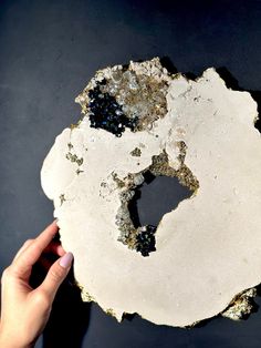 a person holding up a piece of white and black rock with gold flakes on it