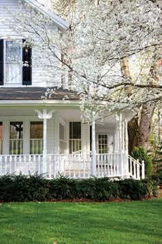 a white house with black shutters on the front porch and trees in blooming