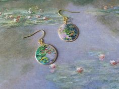 a pair of earrings with flowers painted on them sitting on top of a cloth covered surface