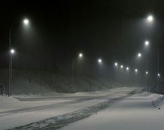 a snowy road with lots of street lights in the night sky and snow on the ground