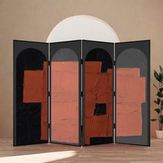 a room divider with an orange and black design on the top, in front of a potted plant