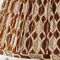 a lamp shade that is on top of a white tablecloth with brown and tan designs