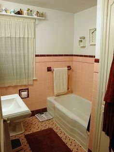 a bathroom with pink tiles and white fixtures, including a bathtub, toilet, sink, and shower curtain