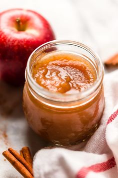 an apple cider in a jar next to cinnamon sticks and an apple on a towel