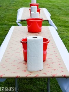 several red buckets are lined up on a long table with toilet paper in them