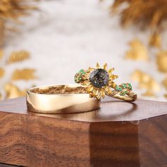 two gold rings with green and white stones on top of a wooden table next to a wall